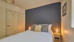 Un dormitorio con cama, lámparas de noche, mesita de noche, una puerta y un cuadro en la pared.