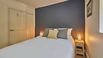 A bedroom with a bed, bedside lamps, a nightstand, a door, and a framed picture on the wall.