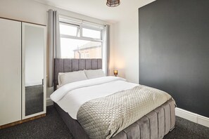 Ein Schlafzimmer mit Bett, Kleiderschrank, Fenster mit Vorhängen und Wand mit Strukturputz.