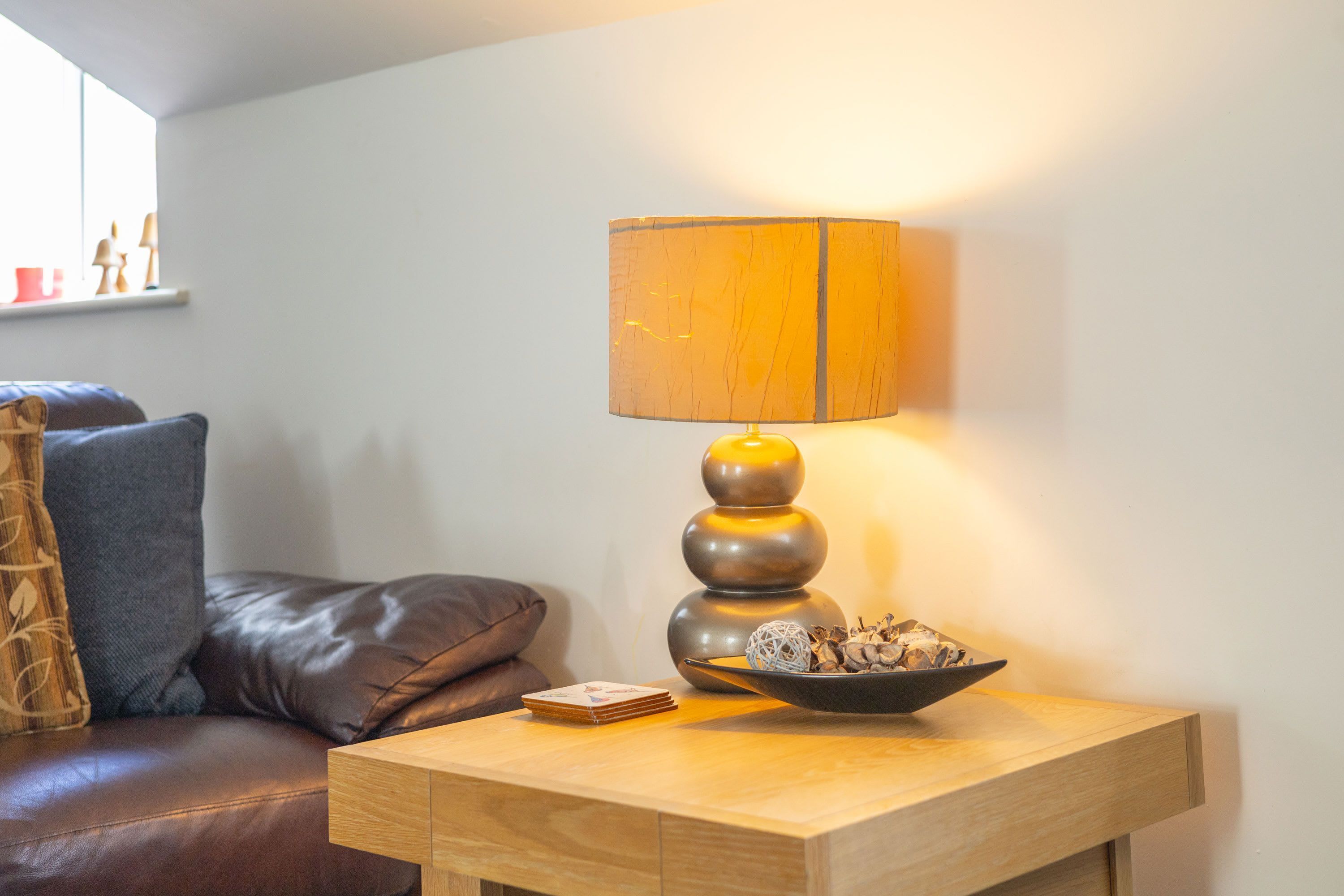 A modern living room with a brown leather sofa, a wooden side table with a lamp and a bowl of decorative items.