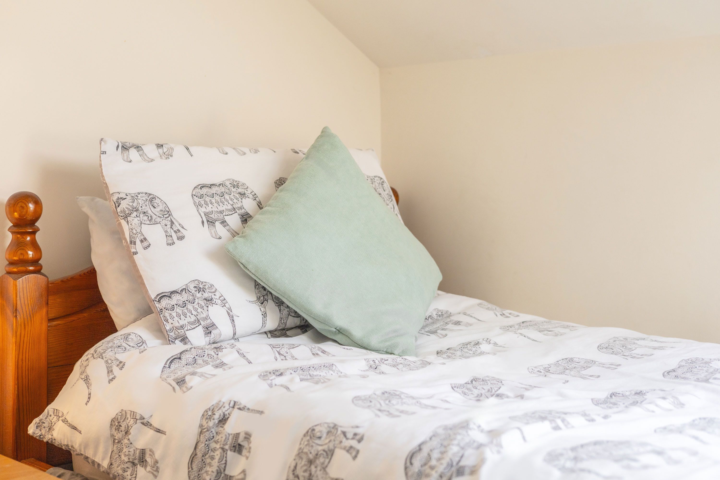 A bed with patterned bedding, a wooden headboard, and a single light green pillow.