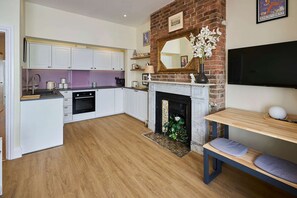 Eine moderne Küche mit weißen Schränken, einem Kamin und einem an der Wand befestigten Fernseher.