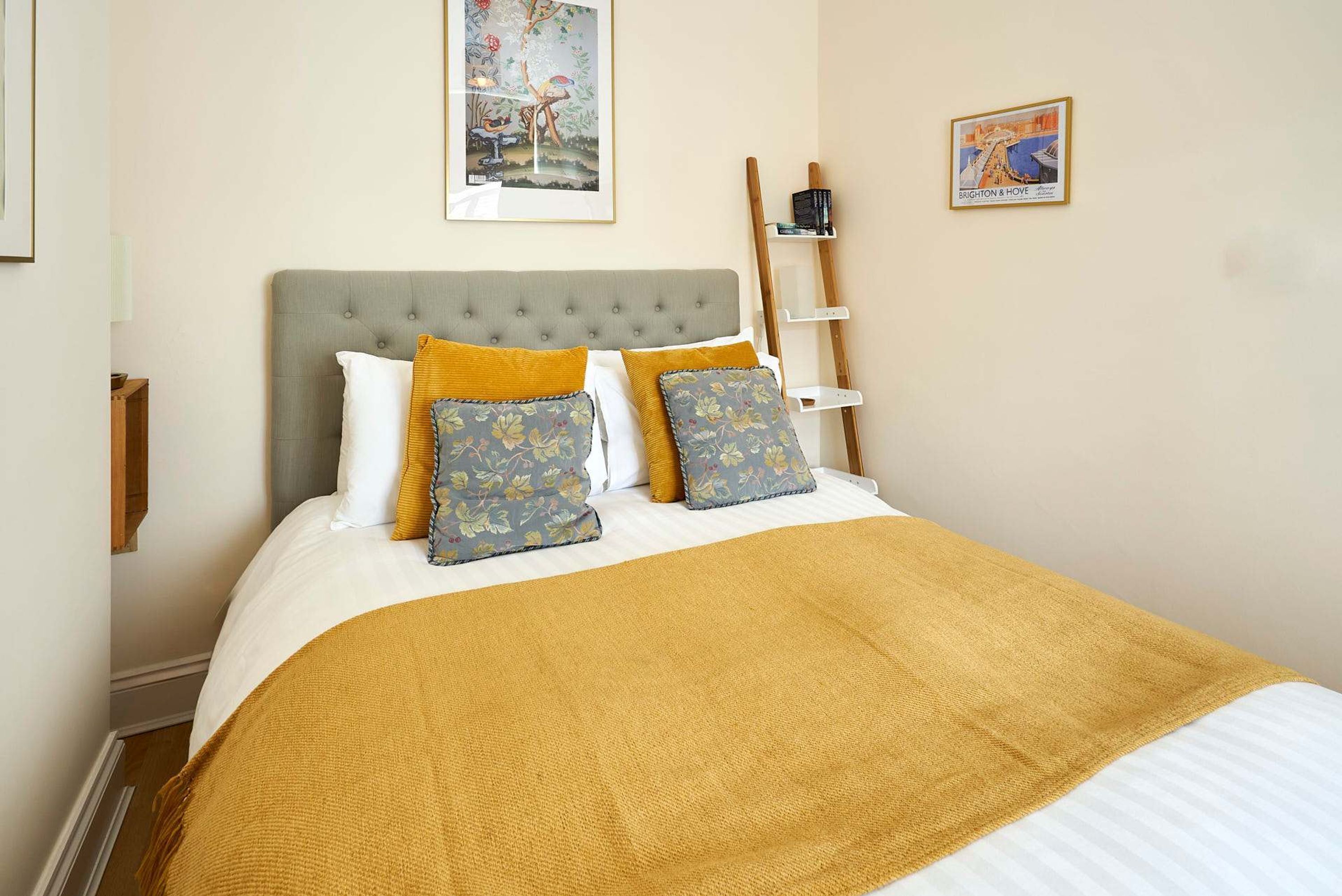 A neatly made bed with a grey headboard, two patterned pillows, and a mustard-colored throw blanket.