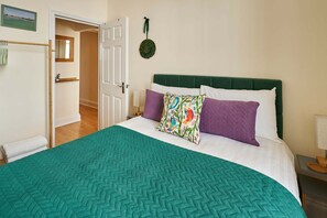 Ein Zimmer mit einem Bett, einem grünen Kopfteil, einer weißen Wand, einer Tür und einem kleinen Fenster.