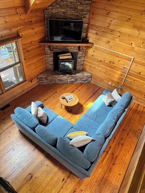 Ein gemütliches Blockhaus-Interieur mit Kamin aus Stein, einem blauen Sofa und einem Holztisch.