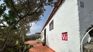 Un edificio blanco con un letrero rojo y blanco, suelo de baldosas de barro cocido y una planta en maceta.