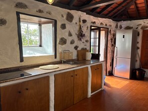 A kitchen with a stone wall, wooden cabinets, a Bosch refrigerator, and a window with a view. - TH - Casa Yerbabuena (Villa de Mazo)