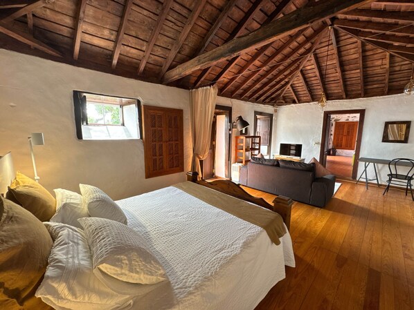 A spacious room with a wooden ceiling, a bed with white linens, a sofa, a television, and a desk. - TH - Casa Yerbabuena (Villa de Mazo)