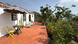 Un edificio blanco con un patio empedrado, sillas amarillas, una mesa y un cactus en maceta.