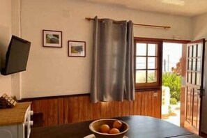 Ein Zimmer mit einer holzgetäfelten Wand, einem an der Wand befestigten Fernseher, einem Fenster mit Vorhang und einem Tisch mit Obstschale.