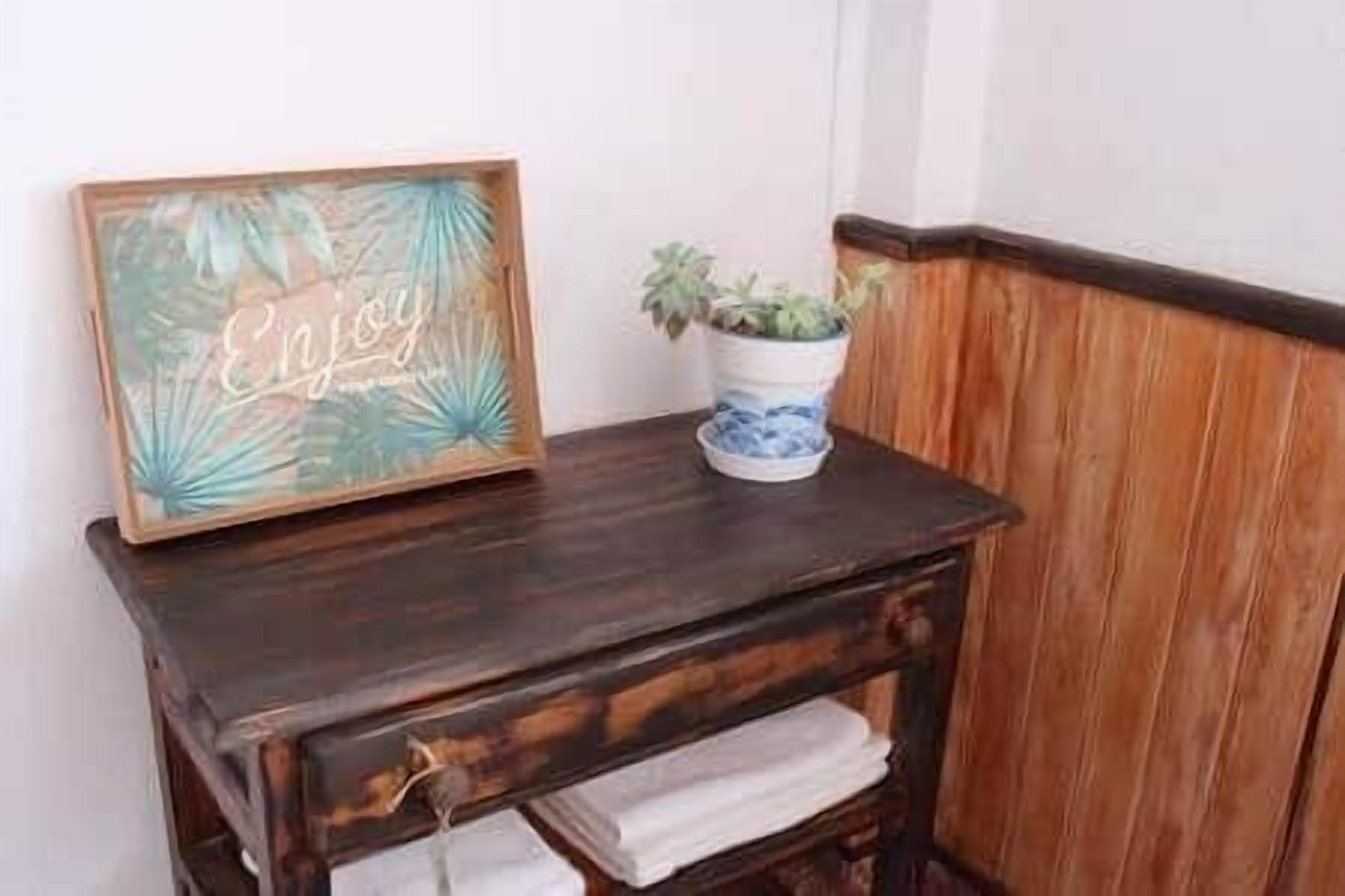 Een houten bijzettafeltje met een lijst, een plant in pot en een handdoek.