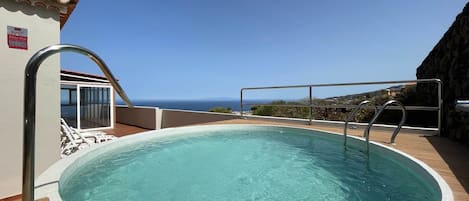 A rooftop swimming pool with a clear view of the ocean, a metal ladder, and a glass door leading to an outdoor area.