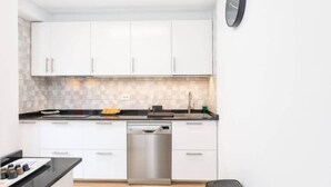 Una cucina moderna con mobili bianchi, una lavastoviglie in acciaio inossidabile e un orologio a parete.