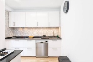 A modern kitchen with white cabinets, a stainless steel dishwasher, and a clock on the wall. - Tendal Duplex - By Tendal Hosting (Santa Cruz de La Palma)