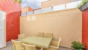Un patio con tavolo e sedie, una pianta in vaso e un muro rosso.