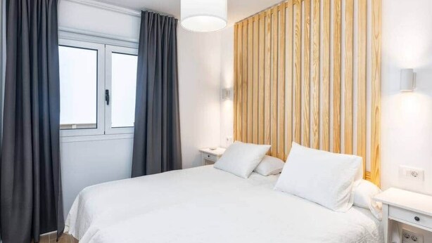 Una camera da letto con un letto, tende, un comodino, una lampada e una parete rivestita in legno.