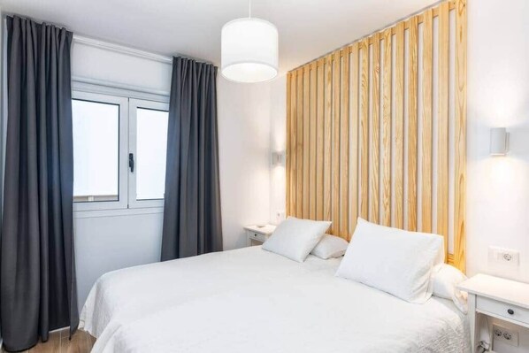 A bedroom with a bed, curtains, a bedside table, a lamp, and a wooden panel wall. - Tendal Duplex - By Tendal Hosting (Santa Cruz de La Palma)