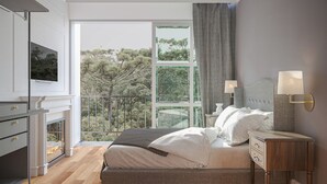 Un dormitorio con cama, lámparas de noche, televisión, chimenea y balcón con vistas a árboles.