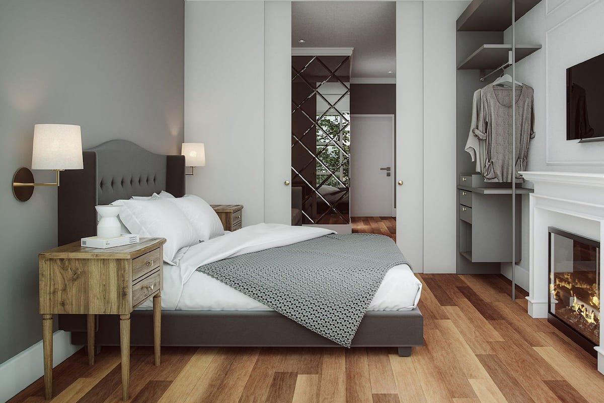 A modern bedroom with a bed, bedside lamps, a wooden nightstand, a grey headboard, a patterned throw blanket, a wardrobe, and a fireplace.
