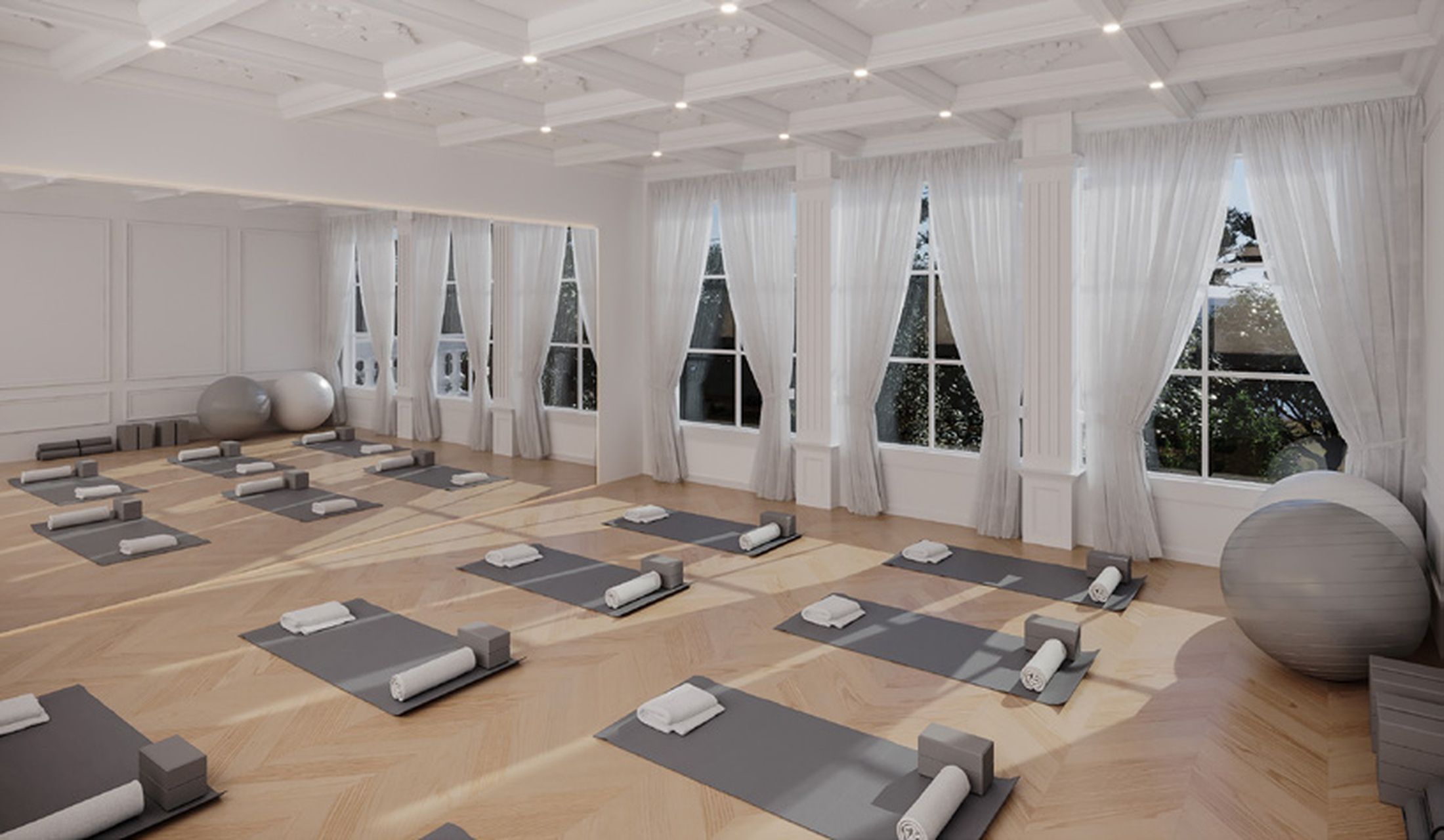 A spacious room with multiple yoga mats arranged for use, large windows with white curtains, and exercise balls.
