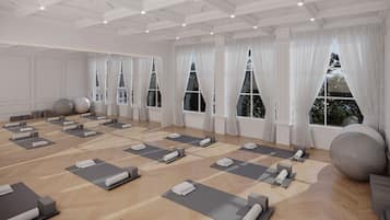 A spacious room with multiple yoga mats arranged for use, large windows with white curtains, and exercise balls.