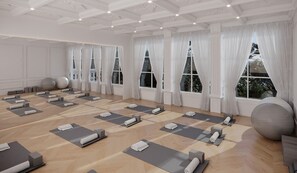 A spacious room with multiple yoga mats arranged for use, large windows with white curtains, and exercise balls.