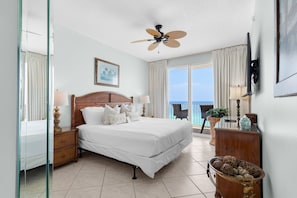 A hotel room with a bed, a ceiling fan, a view of the ocean, and a balcony with outdoor furniture. - Beachfront Bliss, Majestic Sun A1002 | Stunning Gulf Views & Resort Amenities (Miramar Beach)