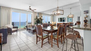 A spacious living area with a large dining table, comfortable seating, and a view of the ocean. - Beachfront Bliss, Majestic Sun A1002 | Stunning Gulf Views & Resort Amenities (Miramar Beach)