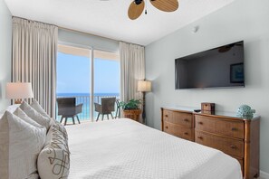 Ein Hotelzimmer mit einem großen Bett, einem Fernseher, einer Kommode und einem Balkon mit Meerblick.