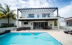 A modern house with a pool, outdoor seating, and a pergola.