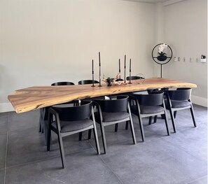 Une table ronde avec un plateau en bois et des chaises noires, placée dans une pièce dont le sol est recouvert de carreaux gris et un des murs est blanc.