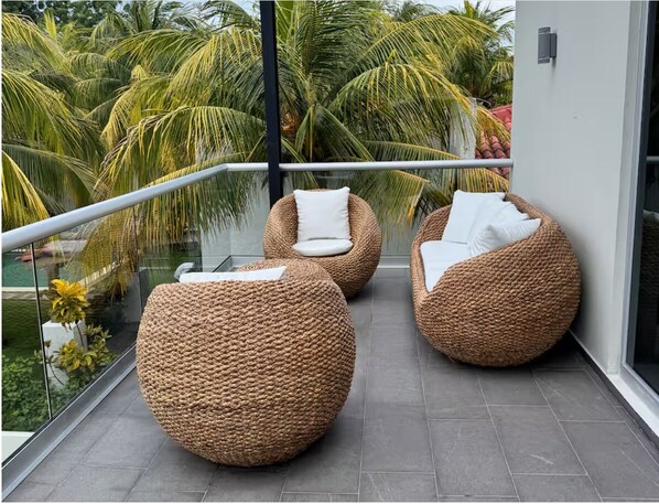A balcony with wicker furniture, glass railings, and a view of palm trees.
