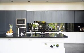 A modern kitchen with dark cabinetry, a stainless steel microwave, and a large island with a black countertop.
