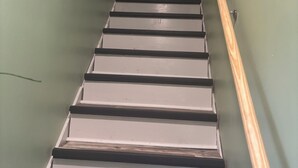 Una scala con gradini in legno e un corrimano, che conduce a una stanza con una parete verde e un arazzo.