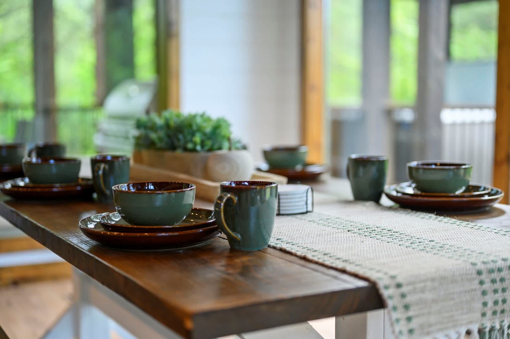 Une table à manger avec des bols et des assiettes en céramique, un set de table en fibres tressées et une plante en pot.
