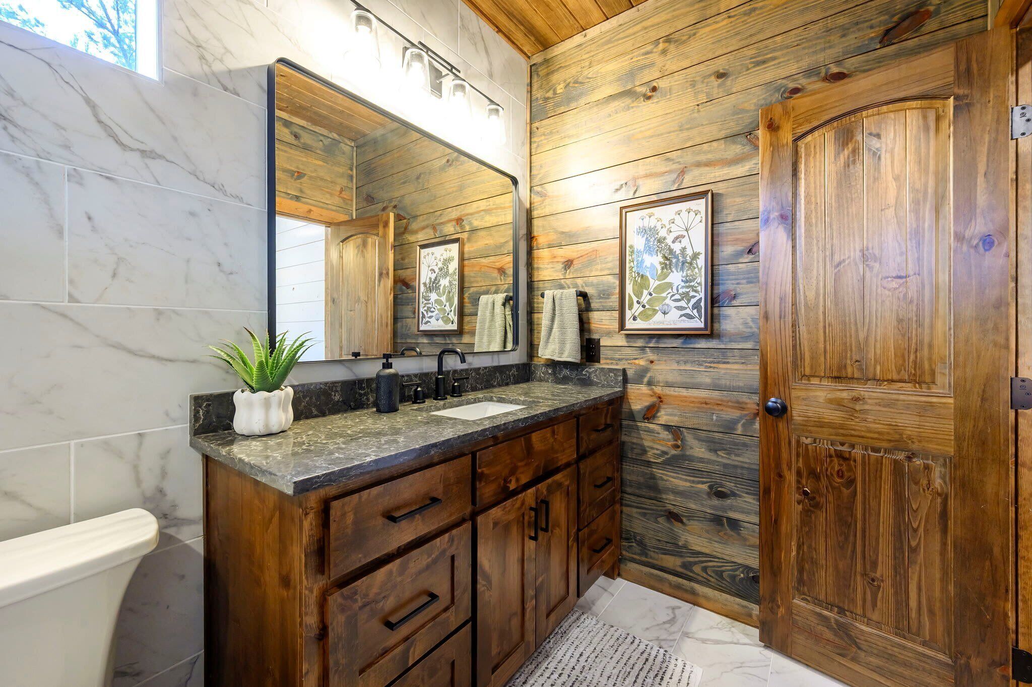 A bathroom with a wooden vanity, marble tiles, a sink, a mirror, and a door.