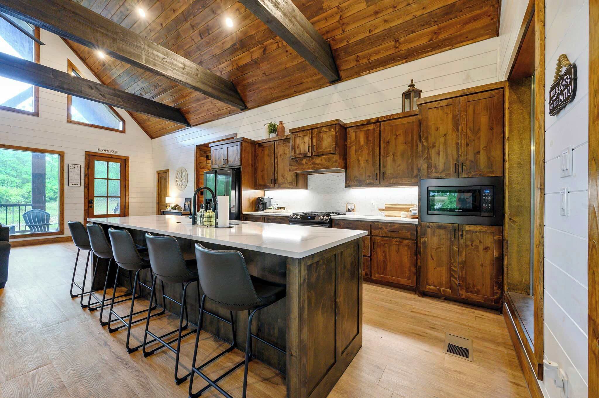 A kitchen with wooden cabinets, a large island with bar stools, a microwave, and a stove.