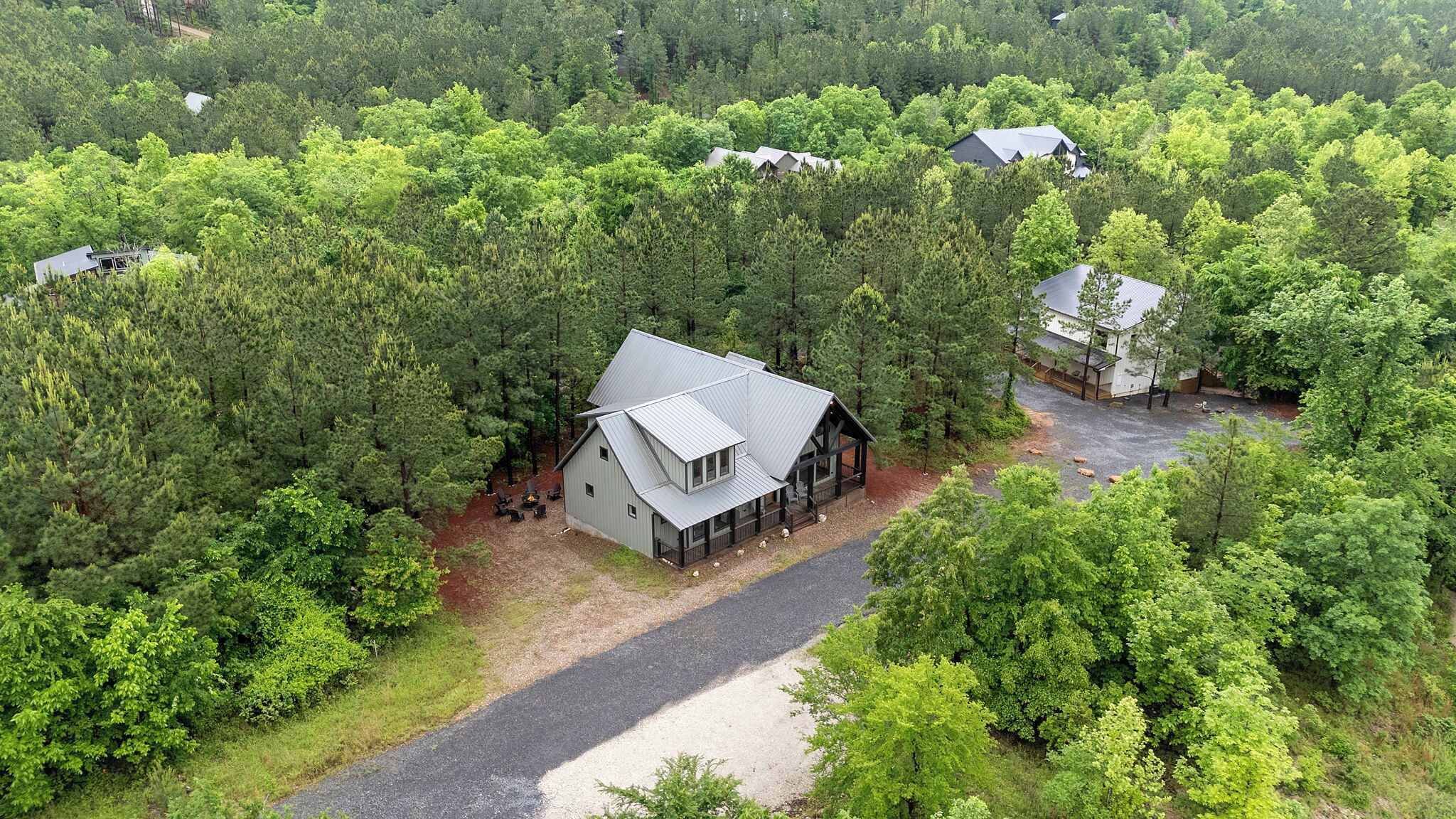 A cabin surrounded by dense forest, with a gravel driveway leading to the entrance.