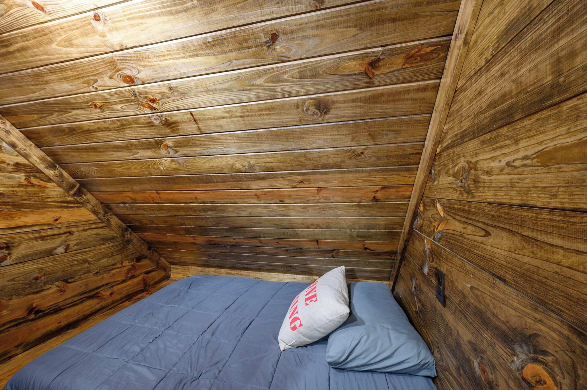 Een houten blokhut van binnen met een enkel bed, een kussen en een hoofdeinde.