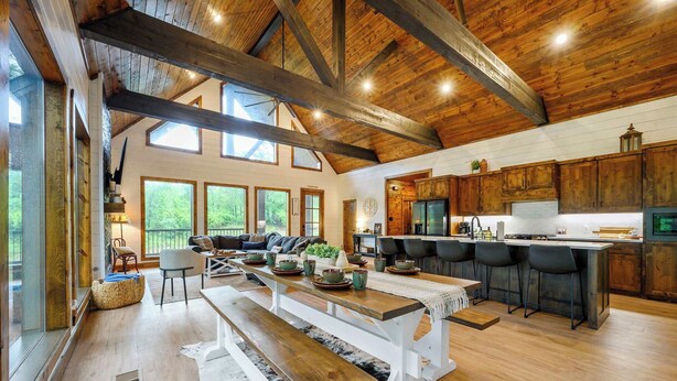 A spacious kitchen with wooden beams, a dining area with benches, and a bar with stools. - Happy Heart Hideaway - Amazing Outdoor Space (Broken Bow)
