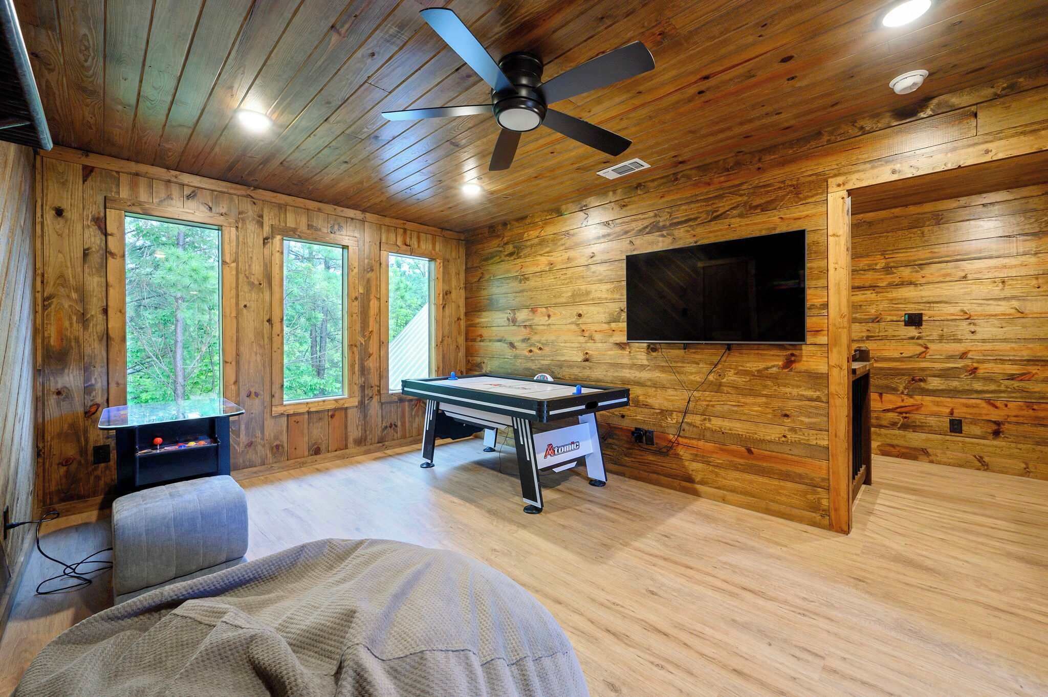 L’intérieur d’un chalet en bois est aménagé avec une table de billard, un ventilateur de plafond, un téléviseur et de grandes fenêtres.