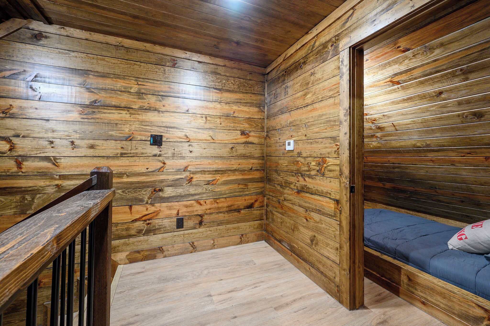 L’intérieur d’un chalet en bois, avec un lit superposé, une rambarde en bois et une petite fenêtre.