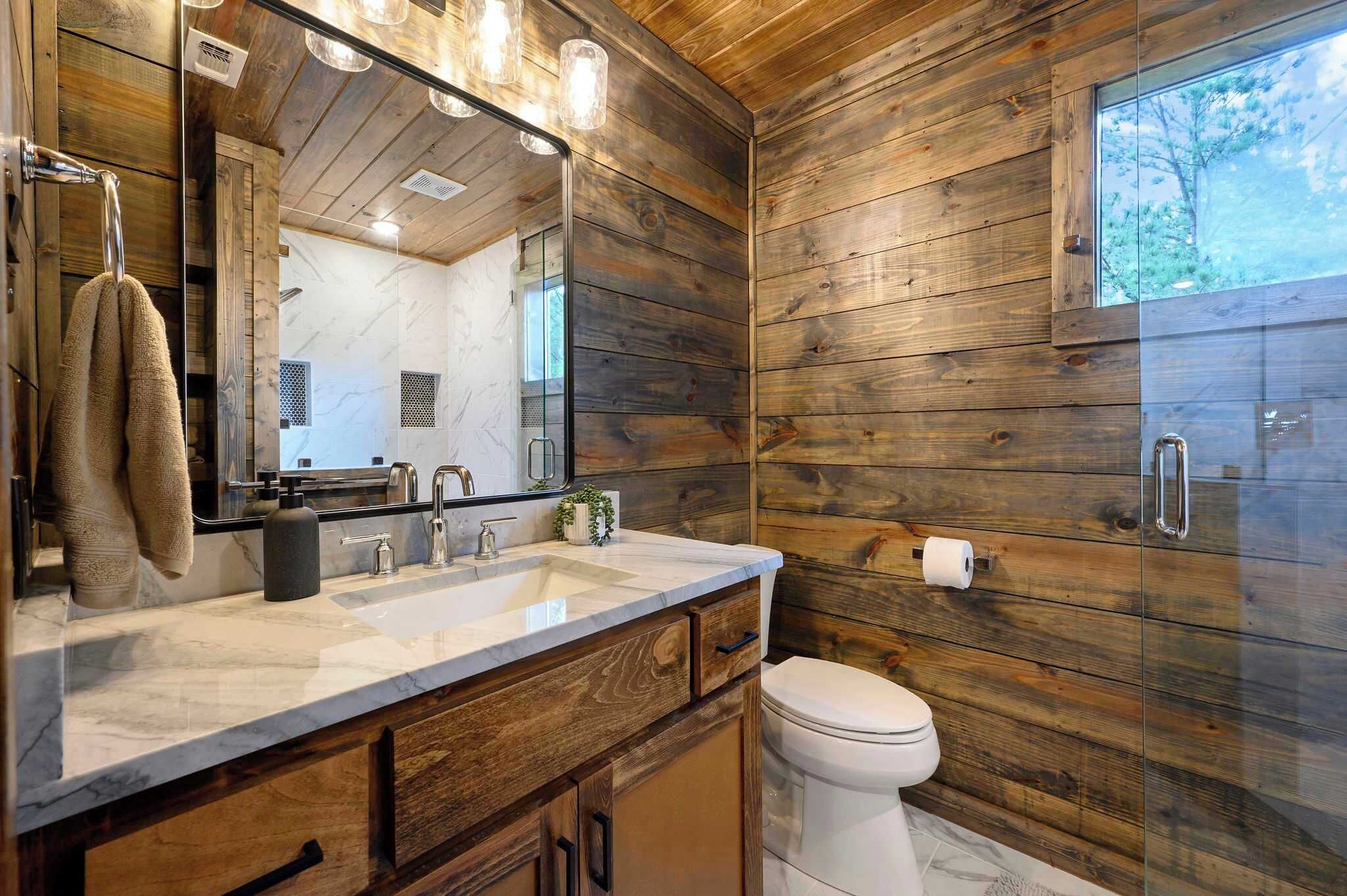 Un bagno con pareti in legno, un lavabo in marmo, uno specchio grande e un water.