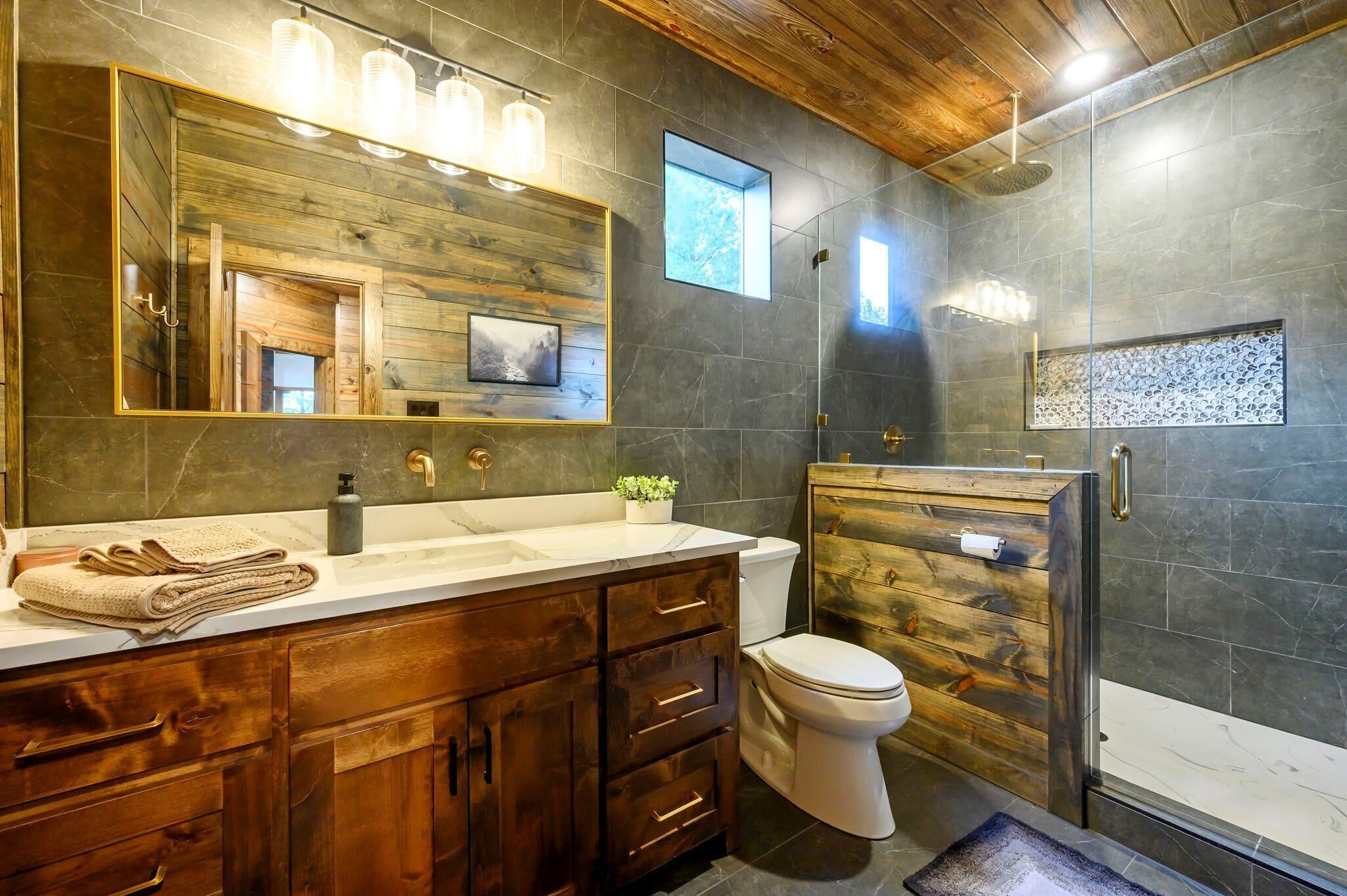 Une salle de bain avec un meuble-lavabo en bois, un grand miroir, des toilettes et un espace douche.
