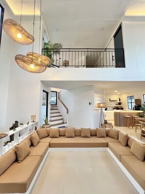 A modern living room with a large sectional sofa, a staircase leading to a balcony, and a kitchen area.