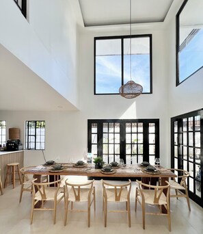 A dining area with a long table, chairs, and a hanging light fixture.