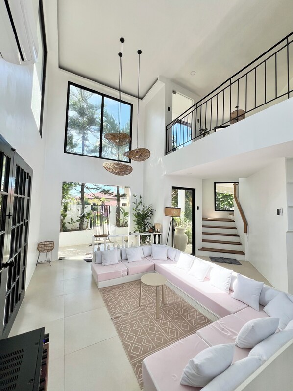A spacious living area with a large L-shaped sectional sofa, a staircase, and a balcony.