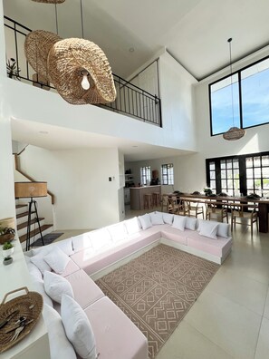 Un espacio habitable amplio con un sofá seccional grande, una mesa de comedor con sillas, una cocina al fondo y un balcón con barandilla.