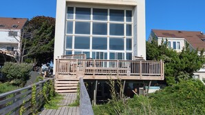 Ein modernes Gebäude mit großem Fenster, einer Holzterrasse und blauem Himmel.
