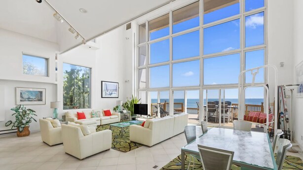 Ein geräumiges Wohnzimmer mit großem Fenster zum Meer, einer Essecke mit Glastisch und einer gemütlichen Sitzgruppe.